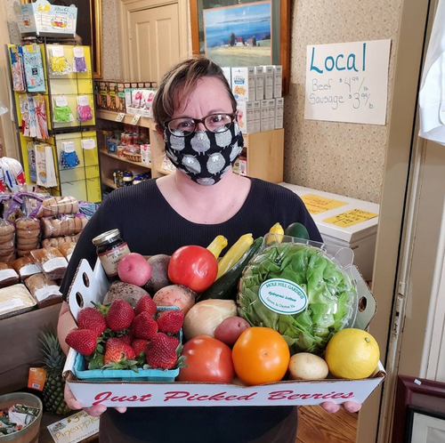person holding a box of local produce including fresh strawberries and tomatoes